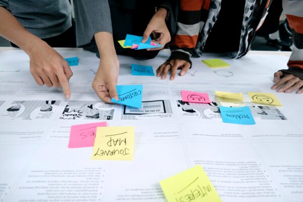 Three sets of hands adding sticky notes to a journey map